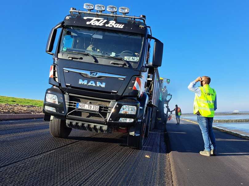 Bauleiter Kilian Efen im Gespräch mit seinem Fahrer. Das Bild zeigt die starke Neigung des Asphaltdeckwerks am Deich. | Foto: DAV/Quillmann