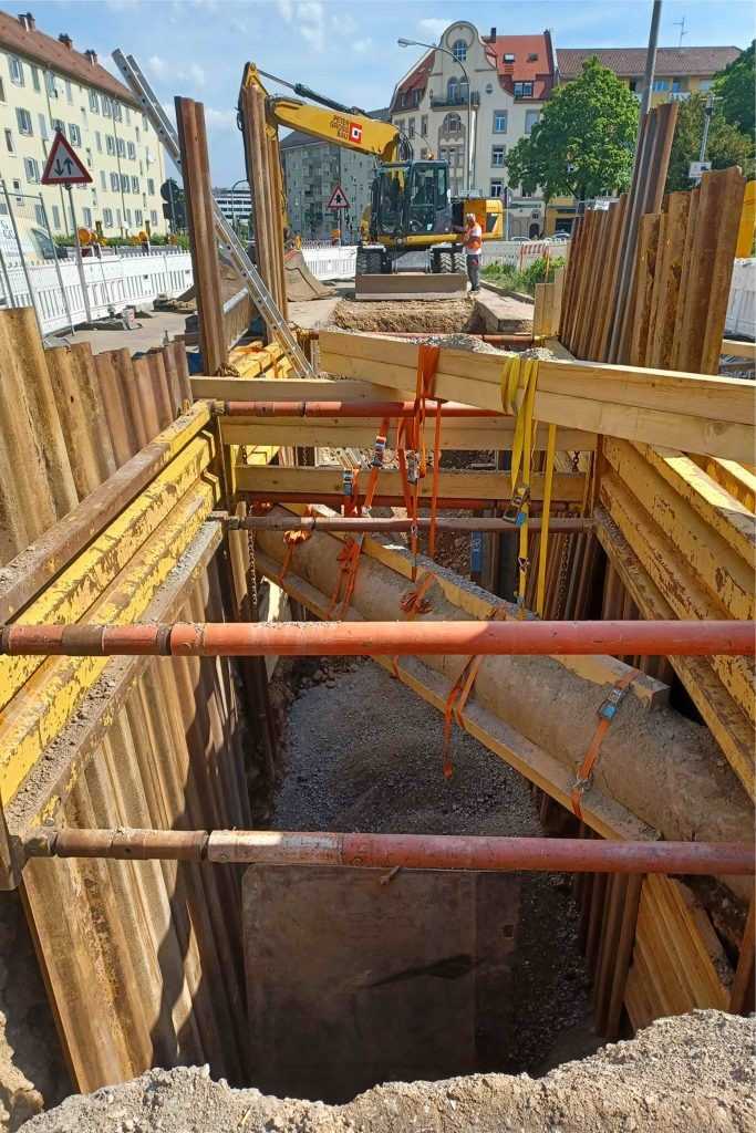 Beim Aushub der Baugrube musste das Erdreich teilweise per Hand entfernt werden, wobei die schließlich frei in der Luft hängenden Rohre weiter versteift wurden und schließlich der Verbau einbaut werden konnte. | Foto: Peter Gross Infrastruktur GmbH & Co. KG