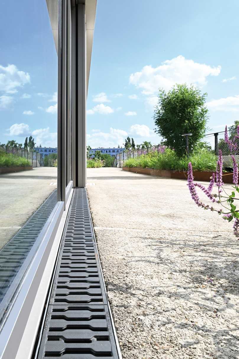 In den Laibungsbereichen an den Türen und Fenstern der Glasfassade stellen die Betonrinnen „Fortis“ zusammen mit den gusseisernen Designrosten „Zippa“ die Entwässerung sicher. | Foto: Richard Brink In den Laibungsbereichen an den Türen und Fenstern der Glasfassade stellen die Betonrinnen „Fortis“ zusammen mit den gusseisernen Designrosten „Zippa“ die Entwässerung sicher. | Foto: Richard Brink