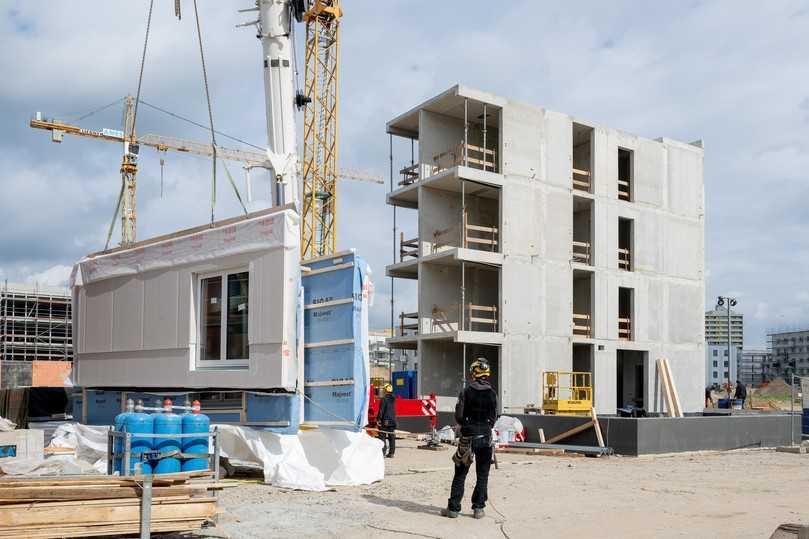 Das erste vorgefertigte Wandelement in Holzrahmenbauweise wird zur Montage versetzt. Rechts der Stahlbetonkern. | Foto: Stadt und Land/Christian Kruppa